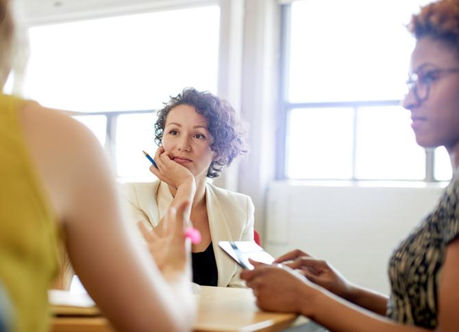 Three women sit in an office meeting.